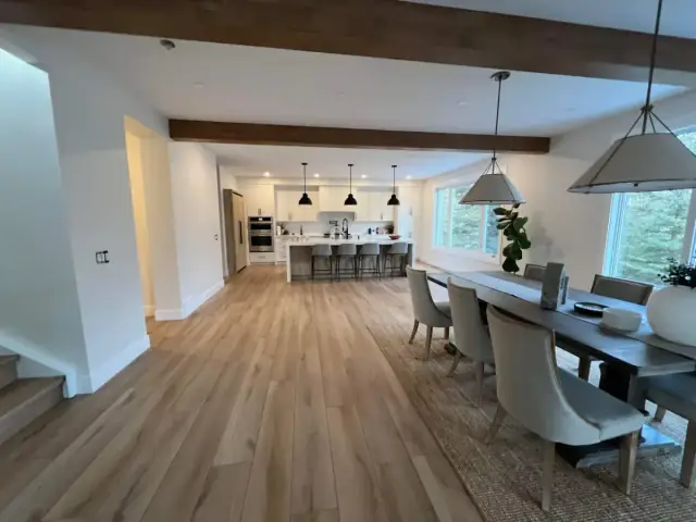 Finished Calgary open-concept living dining and kitchen space with painted walls and wood ceiling beams