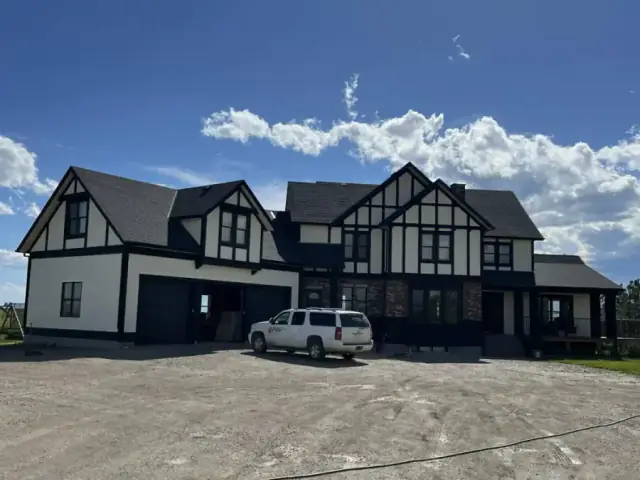 Large black and white stucco estate with dramatic dark trim and Tudor-inspired exterior detailing