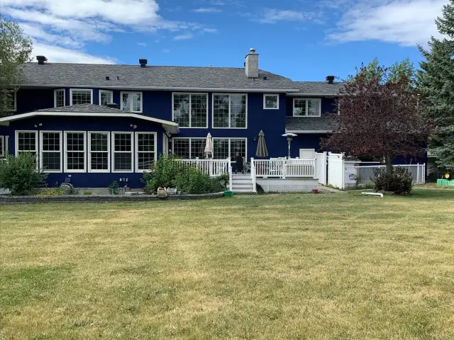 Rear view of large navy blue stucco home with bright white trim and deck