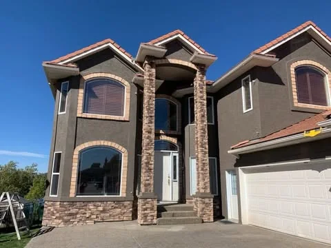 Dark grey two-storey stucco home with stone columns and crisp contrasting garage door