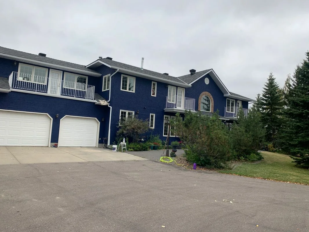 Large Calgary stucco home painted deep navy blue with crisp white trim and garage doors