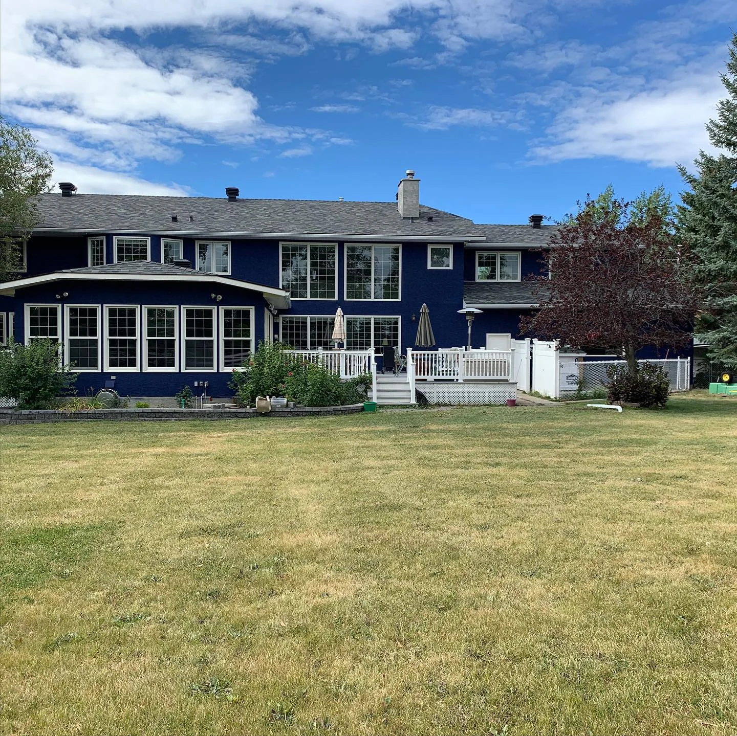 Rear view of large navy blue stucco home with bright white trim and deck