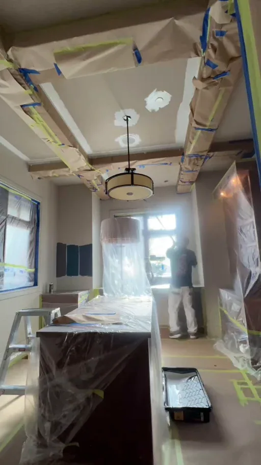 Office ceiling painting in progress with wood beams, windows, desk and flooring covered
