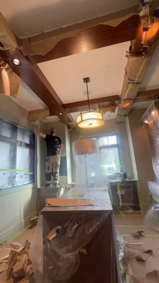 Painter removing masking from the office wood beams after painting, with the desk still protected